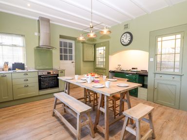 A kitchen with green cabinets a wooden dining table with benches and stools and a green stove at Culdrose Manor in Helston