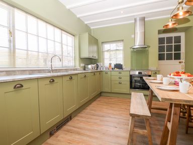 A kitchen with green cabinets a wooden table with cups and plates and a window with blinds at Culdrose Manor in Helston