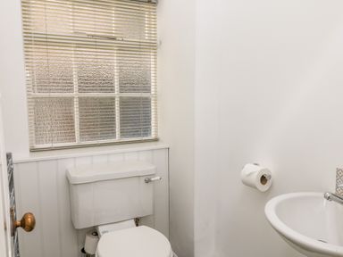 A small bathroom with a toilet under a window and a sink with a faucet on the right side at Culdrose Manor in Helston