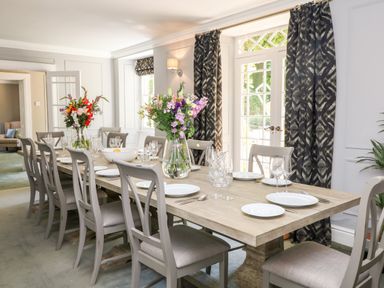 A dining room with a long wooden table set with plates glasses cutlery and flower vases at Culdrose Manor Helston