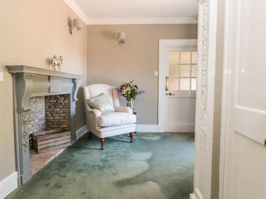 A room with a gray fireplace chair with a pillow flowers in a vase and a white door at Culdrose Manor in Helston