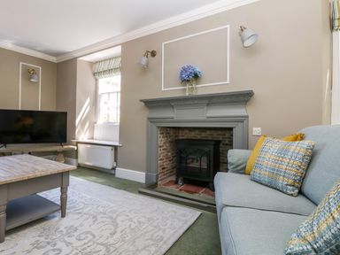 A living room with a fireplace, a light blue sofa with patterned cushions, a wooden coffee table, and a television at Culdrose Manor in Helston