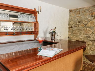 A wooden bar counter with glassware on shelves a bottle in a bucket and an open book on the counter at Culdrose Manor in Helston
