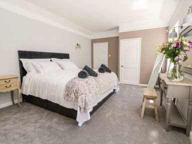 A bedroom with a bed with white linens and dark headboard two bedside tables a console table with a vase of flowers and a full length mirror at Culdrose Manor in Helston
