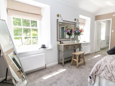 A bedroom with a large mirror on a stand a dressing table with flowers and a wooden stool at Culdrose Manor in Helston
