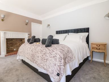 A bedroom with a bed with white sheets and grey rolled towels a wooden bedside table and a white fireplace at Culdrose Manor in Helston