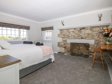 A bedroom with a stone fireplace a bed with white bedding and towels on it two windows with blinds and a wooden stool at Culdrose Manor in Helston