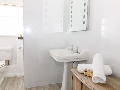 A bathroom with a white toilet a pedestal sink a mirror a wooden cabinet with towels and small bottles at Culdrose Manor in Helston