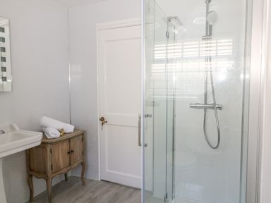 A bathroom with a glass shower enclosure a wooden cabinet with towels on top a sink and a white door at Culdrose Manor in Helston