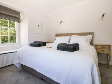A bedroom with a large bed with white bedding two rolled towels on top beside a window and wooden nightstands at Culdrose Manor in Helston