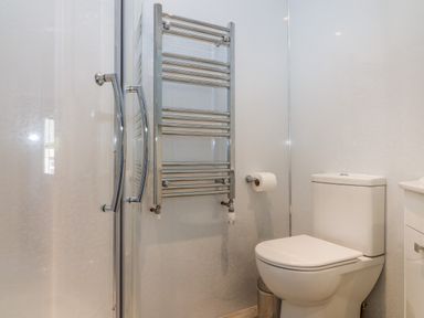 A bathroom with a toilet a towel radiator and a glass shower door at Culdrose Manor in Helston