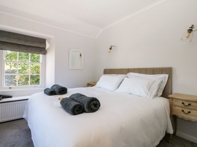 A bedroom with a bed white bedding and dark towels on it two bedside tables a window and wall lights at Culdrose Manor in Helston