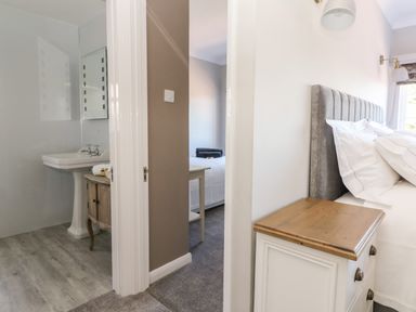 A bedroom with a bedside table next to a bed and a view into a bathroom with a sink at Culdrose Manor in Helston