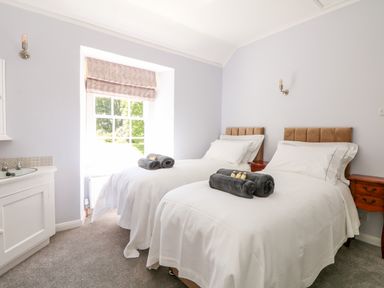 A bedroom with two single beds white bedding wooden bedside tables and a window with a roman blind at Culdrose Manor in Helston