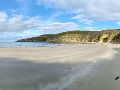 A sandy beach with hills and cliffs under a partly cloudy sky at Nyth Y Wennol in Llanfachraeth
