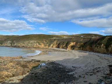 A rocky beach with sand and cliffs under a partly cloudy sky at Nyth Y Wennol in Llanfachraeth