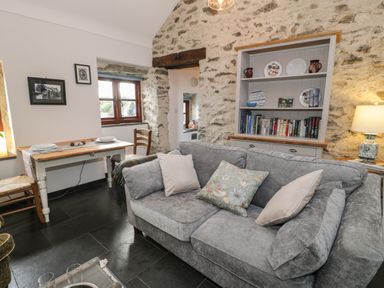 A living room with a gray sofa and cushions a dining table with two chairs and a shelf with books and plates at Nyth Y Wennol in Llanfachraeth