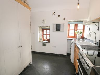 A kitchen with white cabinets a stove a washing machine and windows with wooden frames at Nyth Y Wennol in Llanfachraeth