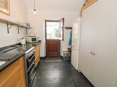 A kitchen with wooden cabinets a stove microwave and refrigerator near a door at Nyth Y Wennol in Llanfachraeth