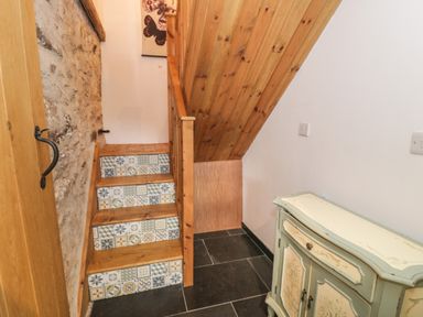 A stairway with patterned tiles on the risers next to a stone wall and a small vintage cabinet at Nyth Y Wennol in Llanfachraeth