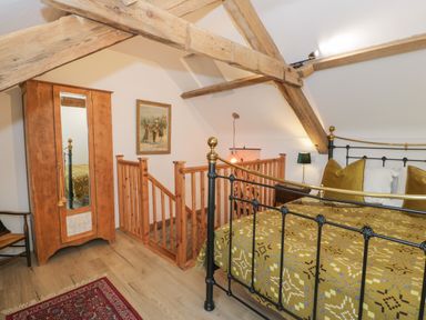 A bedroom with a metal bed frame a wooden wardrobe and a wooden staircase with exposed beams at Nyth Y Wennol in Llanfachraeth