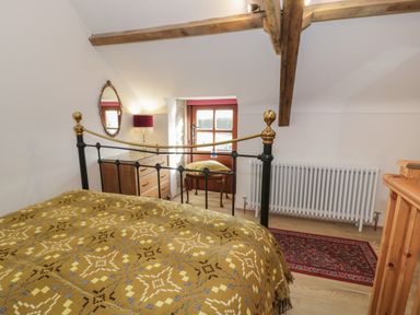 A bedroom with a patterned blanket on the bed a wooden dresser a small table with a cushion on it a mirror and a radiator at Nyth Y Wennol in Llanfachraeth