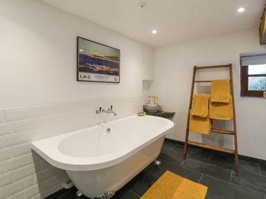 A bathroom with a freestanding bathtub yellow towels on a wooden ladder and a framed picture on the wall at Nyth Y Wennol in Llanfachraeth