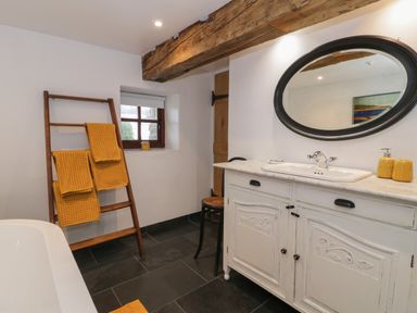A bathroom with a white vanity cabinet and oval mirror a wooden towel rack with yellow towels and a small window at Nyth Y Wennol in Llanfachraeth