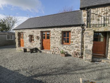 A stone house with wooden doors and windows a bench and metal decorations on gravel at Nyth Y Wennol in Llanfachraeth