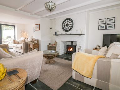 A living room with a stone fireplace clock and couches with a yellow blanket at Hawthorn Cottage in St Teath