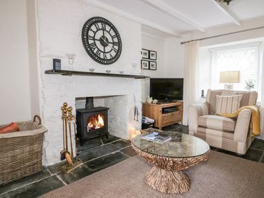 A living room with a fireplace wood stove clock armchair and twig coffee table at Hawthorn Cottage in St Teath