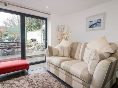 A living room with a striped sofa cushions a red bench shaggy rug and glass doors leading outside at Hawthorn Cottage in St Teath