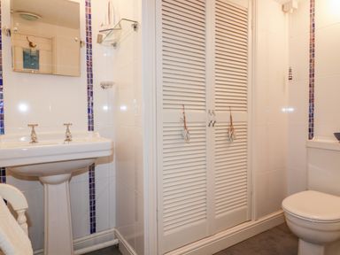 A bathroom with a pedestal sink toilet and white louvered closet doors at Hawthorn Cottage in St Teath