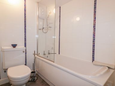 A bathroom with a toilet a bathtub with a glass shower screen and tiled walls at Hawthorn Cottage in St Teath