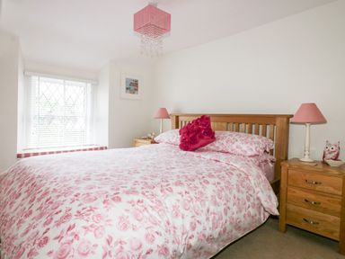 A bedroom with a wooden bed with floral bedding and two wooden bedside tables with pink lamps at Hawthorn Cottage in St Teath