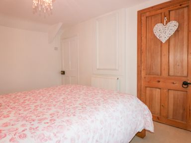 A bedroom with a floral patterned bedspread two wooden doors and a chandelier at Hawthorn Cottage in St Teath