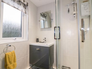 A bathroom with a window, a sink with cabinet, a mirror, a shower enclosure, and a yellow towel at Hawthorn Cottage in St Teath