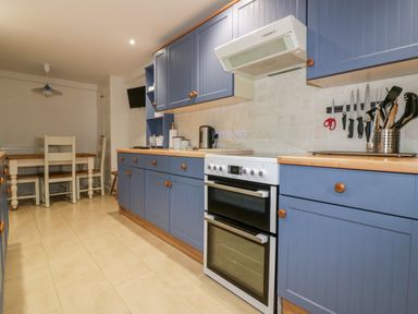 A kitchen with blue cabinets a white oven a dining table with chairs and kitchen utensils at Hawthorn Cottage in St Teath
