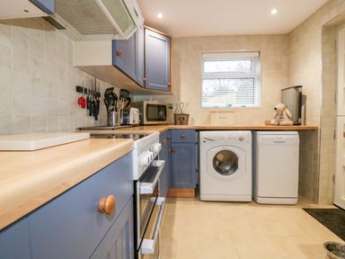 A kitchen with blue cabinets a washing machine a dishwasher a stove microwave and utensils on the counter at Hawthorn Cottage in St Teath