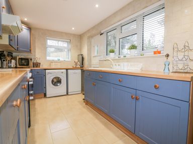 A kitchen with blue cabinets appliances and windows with blinds at Hawthorn Cottage in St Teath