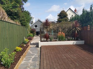 A garden with a wooden deck stone path and plants along fences at Hawthorn Cottage in St Teath