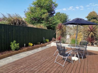 A patio with a round glass table and four chairs under a black umbrella at Hawthorn Cottage in St Teath