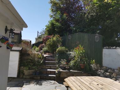 An outdoor garden area with stone steps plants wooden table and a white wall at Hawthorn Cottage in St Teath