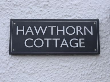 A black and white sign reading hawthorn cottage on a textured white wall at Hawthorn Cottage in St Teath