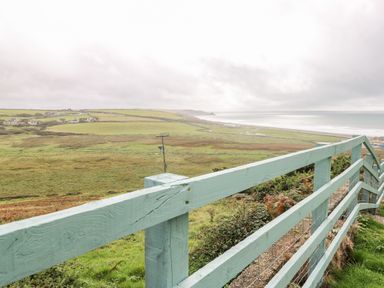 A coastal landscape view with green fields and a blue wooden fence at Valley High in Solva