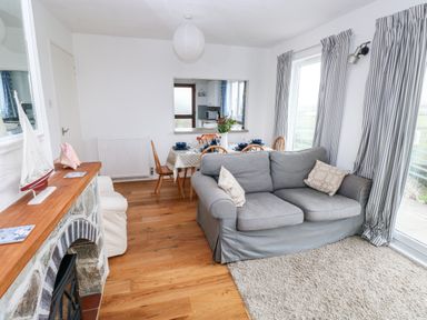 A living room with a gray sofa next to windows with striped curtains a dining table set for four and a fireplace with a model sailboat at Valley High in Solva