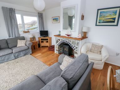 A living room with grey sofas a white armchair a stone fireplace TV and wooden furniture at Valley High in Solva