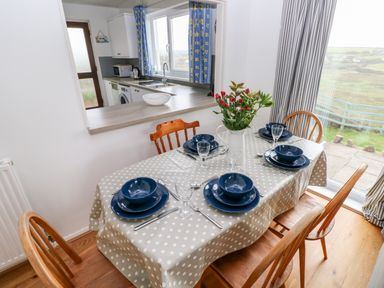 A dining area with a table set for four with blue dishes and a vase with flowers near a large window and a kitchen with a counter in the background at Valley High in Solva
