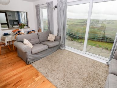 A living room with two sofas a dining table set with dishes and large windows showing a countryside view at Valley High in Solva