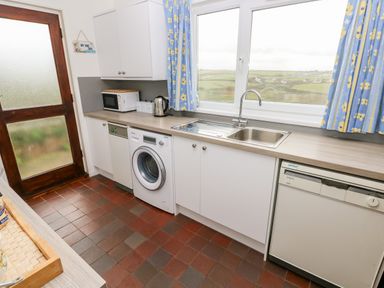 A kitchen with white cabinets a washing machine dishwasher microwave kettle and a sink with a window showing countryside at Valley High in Solva
